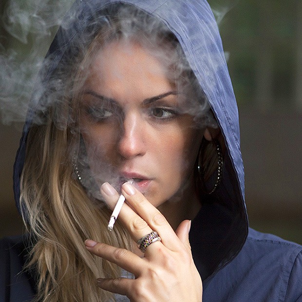 Young adult woman in hood smoking a cigarette