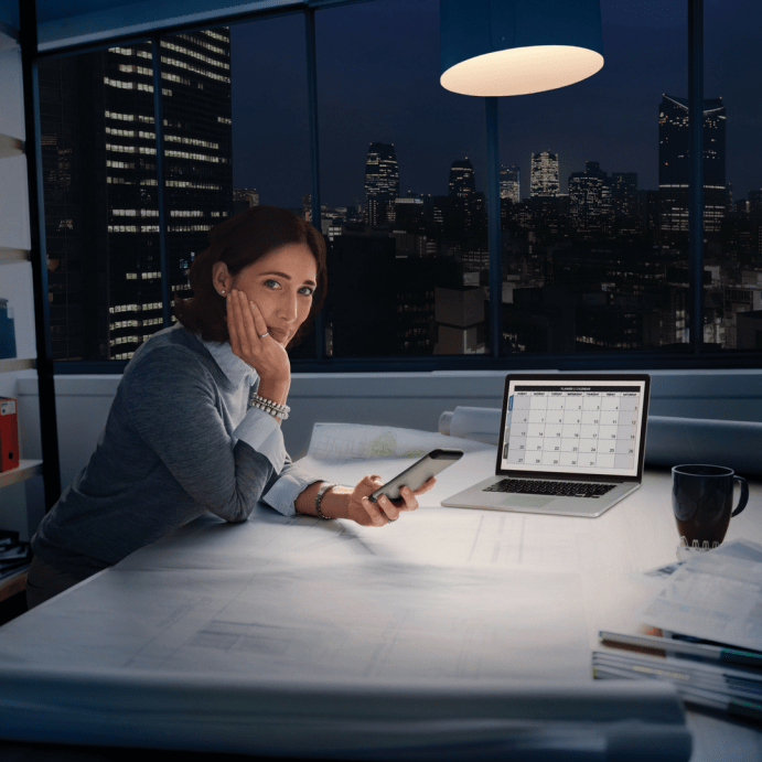 Woman holding a phone sitting at desk, looking at camera