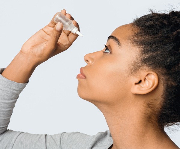 Young woman applying eyedropper, gray background